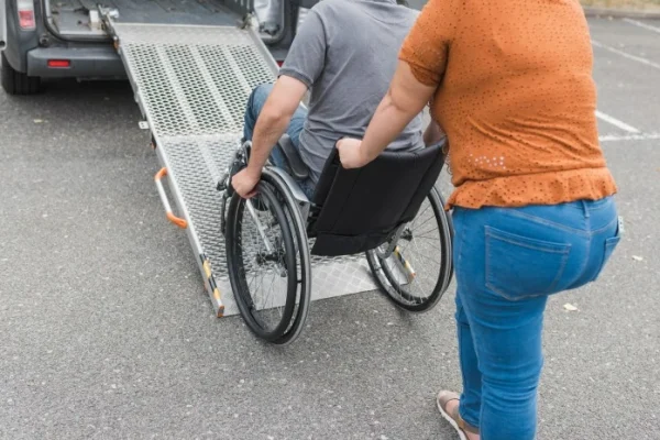 Support worker pushing disabled man up ramp into van