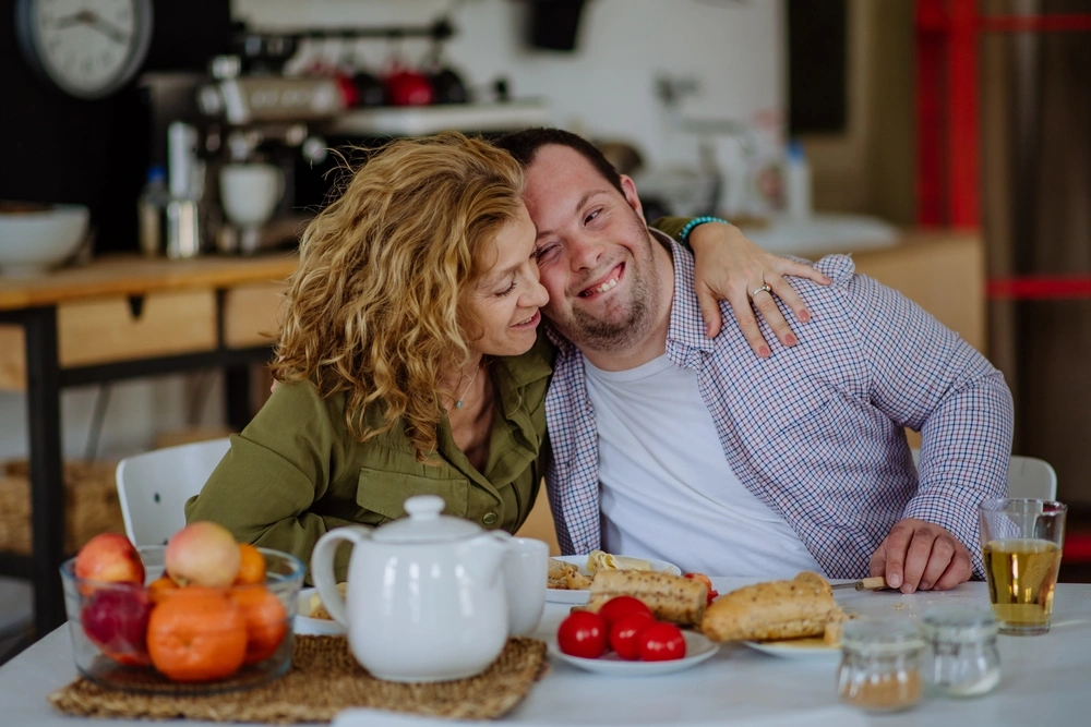 Mum hugging disabled son at kitchen table