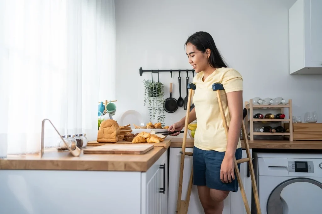 Disabled woman with amputated leg using crutches in kitchen