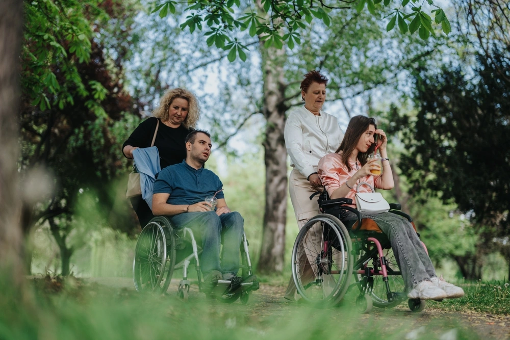 Two disabled friends in wheelchairs with support workers